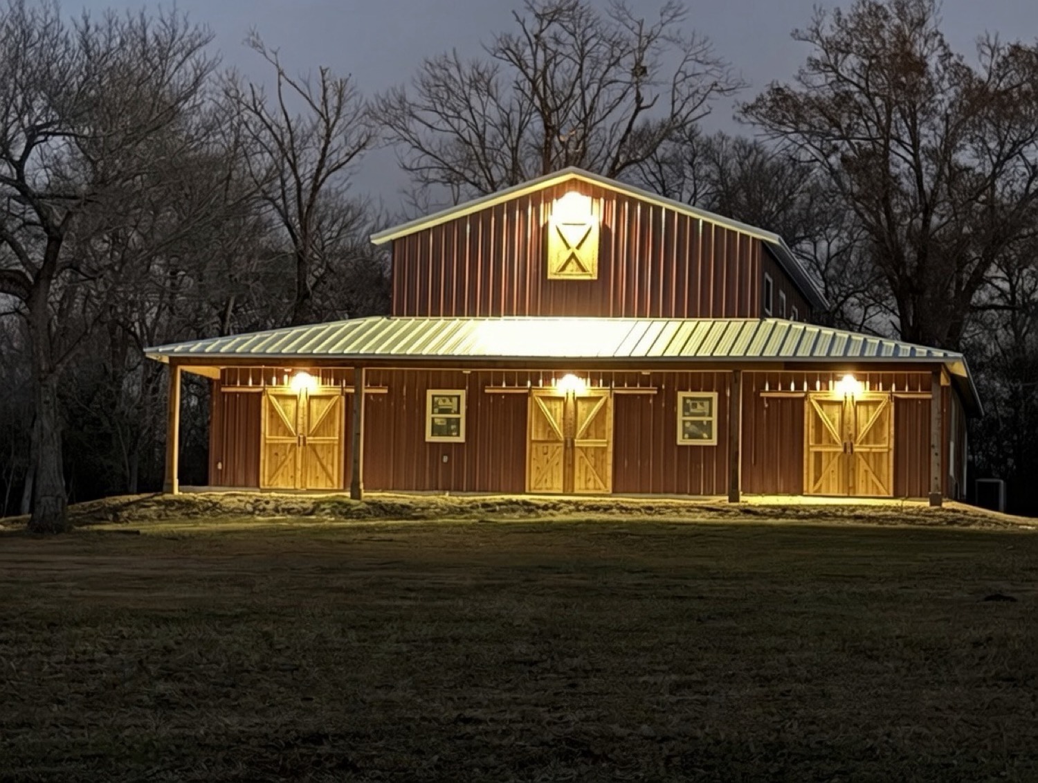 The red barn at night, porch lights on and the loft glowing